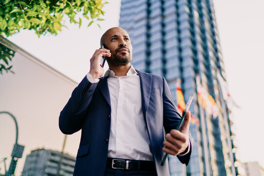 Businessman talking on smartphone, holding digital tablet, expressing executive clarity, multitasking skill and international business fluency.
