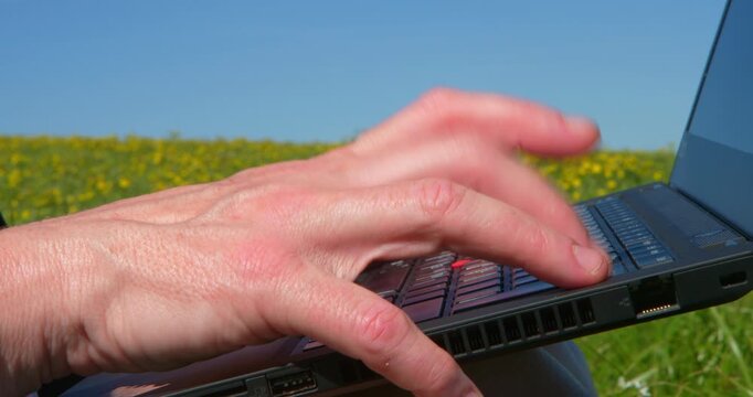 Digital Field Office: A person's hand swiftly navigates a laptop keyboard set against a vivid natural landscape. This image captures the seamless integration of technology and the outdoors.