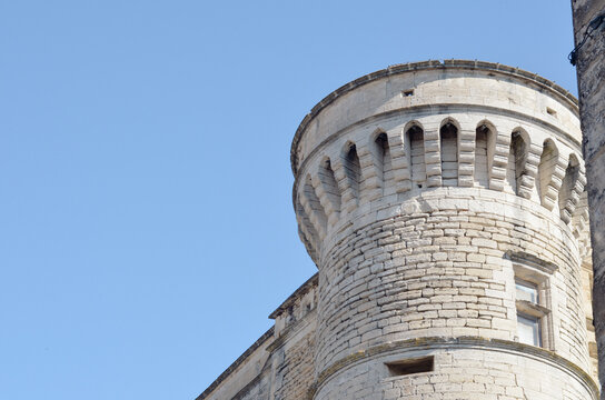 Ancient round stone tower of a medieval fortress against a clear blue sky. Traditional Mediterranean architecture with stone masonry and defensive machicolations in Provence style, France.