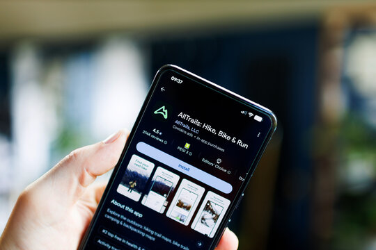 mobile phone in hand with AllTrails Hike Bike and Run app on the google play store
