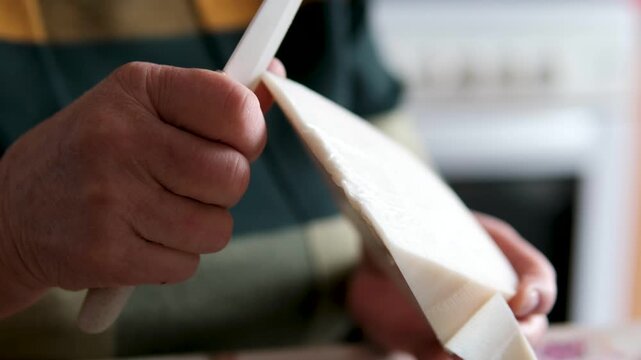 An elderly woman hands prepare cheese for serving, removing it from packaging and placing. wooden cutting board. Close-up of a homemade kitchen moment as she slices cheese for her grandchildren.