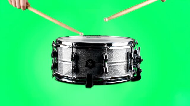 A close-up shot of a metallic snare drum being struck by drumsticks against a chroma key green screen background. This clip is ideal for music production, rhythmic synchronization, band promotions, or