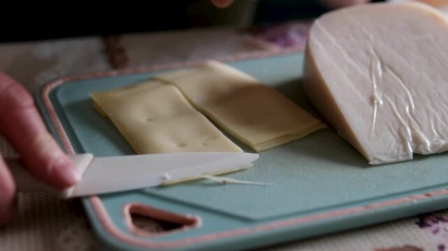 Pre-sliced packaged cheese is being arranged on plates, with sheep cheese placed on an old plastic board nearby. Close-up of a home kitchen scene highlighting dairy foods rich in calcium and simple.