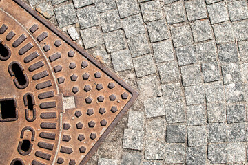 Granite cobblestone pavement with rusted metal drain cover, urban texture background with diagonal composition and copy space © varbenov