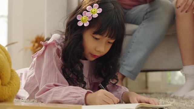 Little Asian girl drawing on floor with parents watching in background