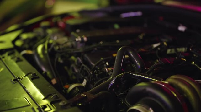 Slow motion close-up of a high-performance, tuned car engine with a large turbocharger, illuminated by vibrant green and magenta lights in a workshop, ready for racing or street drag