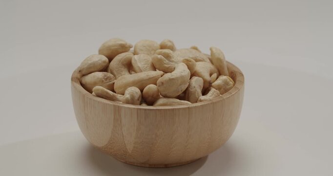 Rotating small wooden bowl filled with raw cashew nuts isolated on a white background, presenting a healthy and nutritious snack option for a balanced diet and vegan lifestyle.