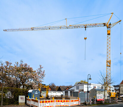 G&uuml;tersloh,Deutschland 03.04.2026- Baukran auf einer Baustelle. Im Vordergrund DIXI-WC-H&auml;uschen unter bl&uuml;henden Magnolienbaum, neben Absperrbaken und Bauwagen und gelben Bagger