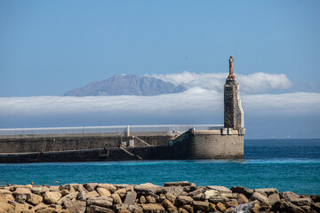 Espigón con estatua y montaña entre nubes sobre mar turquesa © Adrian