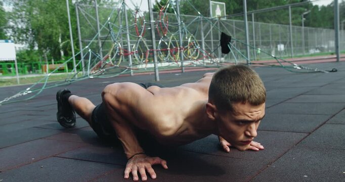 Man with athletic body has morning workout outdoors and doing push up exercise. Sporty guy training arms muscles at sport ground. Sportsman muscular strong guy bodybuilder do push-ups exercise.