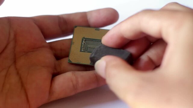 Close up of a hand cleaning golden CPU processor pins using a white eraser. Concept for computer hardware maintenance, repair, and DIY PC troubleshooting.