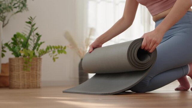 Hands of Asian woman rolling grey yoga mat after fitness class
