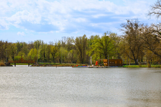 Lake in the S&aacute;rv&aacute;r park in Hungary with spring trees, calm water, wooden boathouse and colorful kayaks creating a peaceful recreational landscape