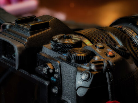 Close up of mirrorless camera controls and lens with mode dial and record button in warm low light professional photography equipment