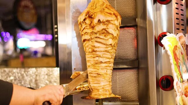 Chef slicing meat from vertical rotisserie cooking for shawarma or d&ouml;ner kebab dish.
