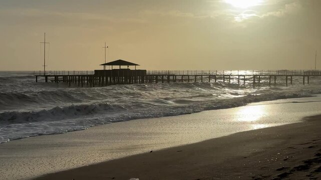 Sunset over calm beach scene with a pier and gentle waves, ideal for background or tropical themes