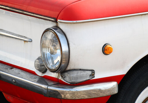 Detail of bumper and front round headlight of old red car. Closeup side view.