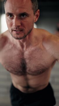 Determined middle-aged man with a muscular physique doing chest exercises on a cable crossover machine. Intense workout session focusing on strength, endurance, and muscle building in a modern gym