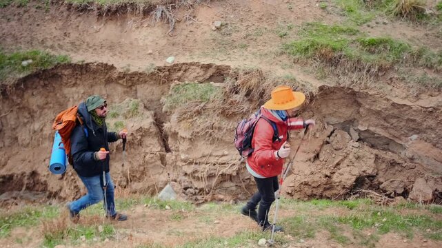 two hikers moving carefully along edge of ravine, avoiding steep drop and choosing safer route, showing awareness and decision making during challenging mountain trekking