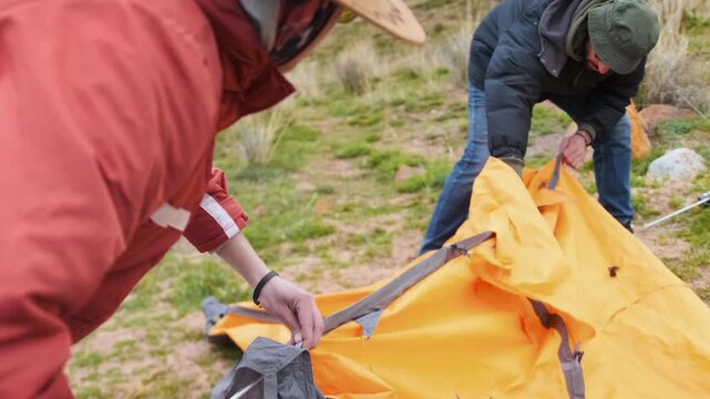 two hikers assembling tent and preparing campsite in natural environment, teamwork and cooperation during outdoor adventure, concept of preparation, survival and travel routine