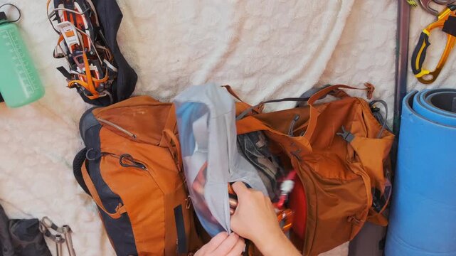 top view man packing climbing gear into backpack, organizing mountaineering equipment hiking trip, preparing for outdoor adventure, travel and expedition preparation. Male hands packing climbing gear