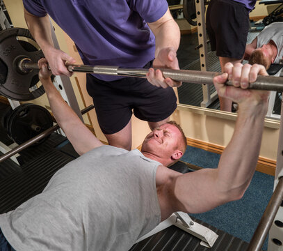 Man lifting weights on bench press at gym with spotter
