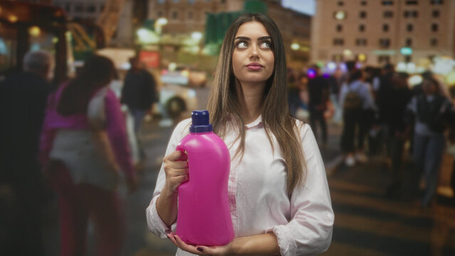 Woman holding bright pink detergent bottle with right hand on a crowded urban street, looking up while cradling the jug; practicality calm.