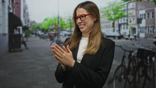 Woman pinching nose with both hands on a busy city street wearing red glasses and black blazer grimacing from a foul smell; unpleasant smell disgust.