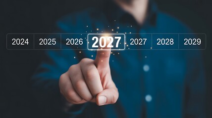 Obraz premium A person's hand touches a glowing digital interface displaying the year 2027, symbolizing future vision, strategic planning, and upcoming opportunities