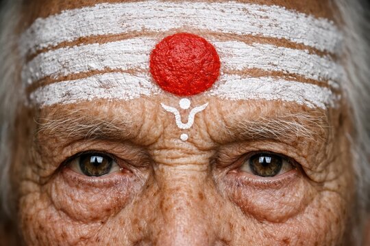 Intense closeup of an elderly Indian man wearing tripundra and trishul tilak, highlighting age, devotion, and facial texture.