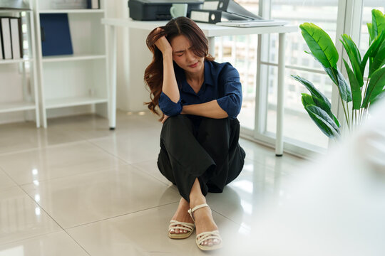Exhaustion and Overwhelm in the Office: A woman sits dejectedly on the floor, head in hand, her posture reflecting feelings of exhaustion and stress.