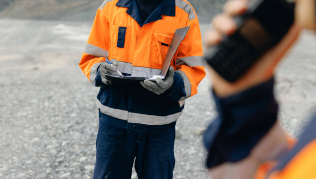 Geologist holding clipboard inspecting rock ore sample at mining excavation site