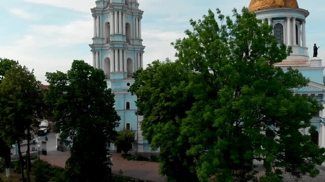 Drone shot of the Transfiguration Cathedral in Sumy, Ukraine, showing the detailed bell tower with a golden dome in the central city square. In the background is the Resurrection Cathedral