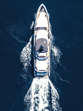 Aerial view of a luxury white yacht cruising through deep blue water leaving a white wake.