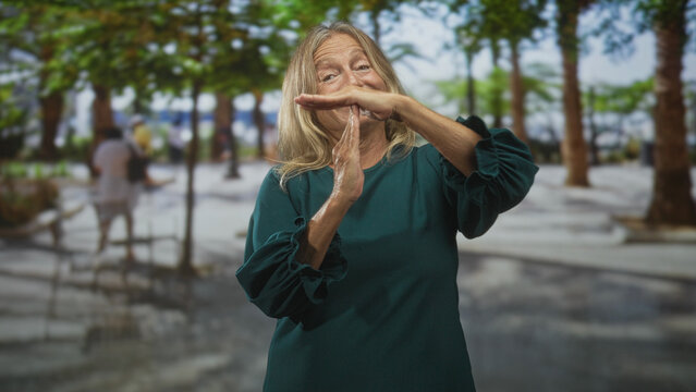 Senior woman making timeout hand gesture with hands held near face on a tree lined street; calm pause.