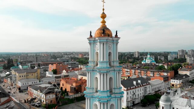 Drone shot of the Transfiguration Cathedral in Sumy, Ukraine, showing the detailed bell tower with a golden dome in the central city square. In the background is the Resurrection Cathedral