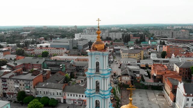 Close aerial drone view of the Transfiguration Cathedral in Sumy, Ukraine, featuring a detailed bell tower with a golden dome and classical architecture in the central city square
