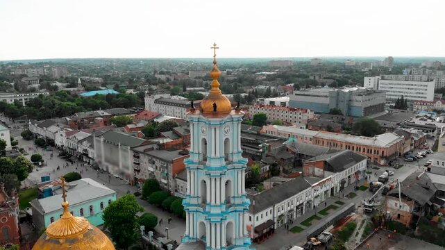 Close aerial drone view of the Transfiguration Cathedral in Sumy, Ukraine, featuring a detailed bell tower with a golden dome and classical architecture in the central city square