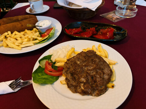 Traditional Serbian dishes pljeskavica and Karadjordjeva schnitzel served with fries, vegetables and roasted peppers in a restaurant. Concept of Balkan cuisine, dining and local food experience.