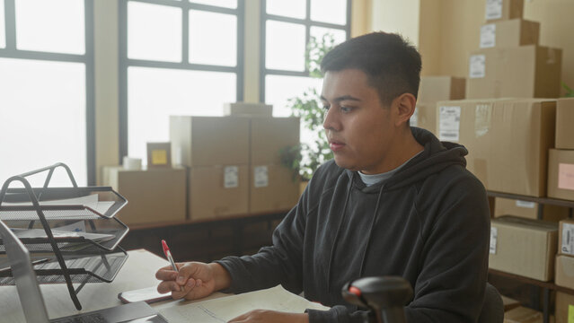 Man hand writing with pen at laptop among stacked parcels in a building; small business focus efficiency.