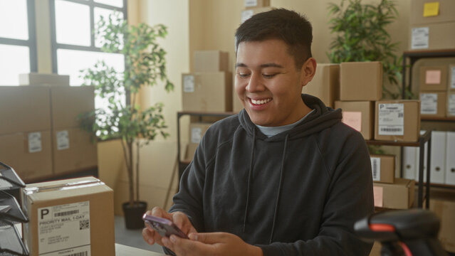 Man holding smartphone and tapping screen in building office with delivery parcels; small business joy.