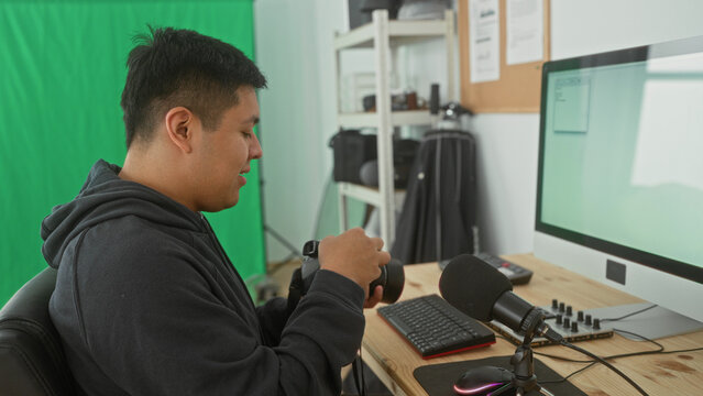 Man adjusting camera at studio desk with green screen, computer and microphone; concentration craft creativity.