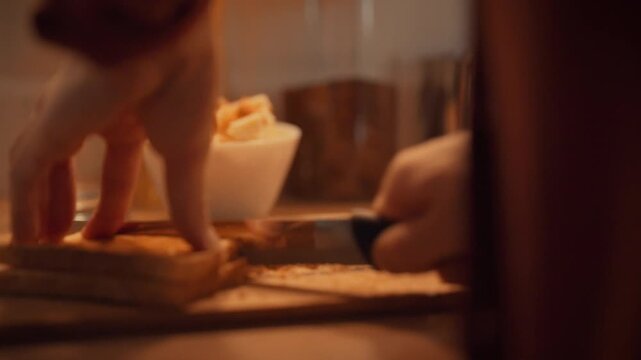 In cozy kitchen, man skillfully slices toasted bread into croutons using sharp knife on table, preparing breakfast treat. toaster-fresh bread is transformed into crunchy morsels for culinary delight
