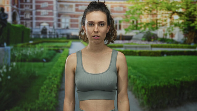 Hispanic young woman covers mouth with hand for silence outside building as she gazes forward; shock.