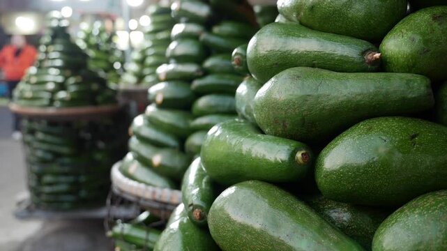 Avocados are stacked in pyramid rows on a market stall counter forming an organized fresh produce display in an outdoor trading environment. Fresh produce.
