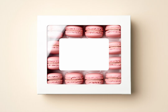 White box with transparent window and blank label filled with pink macarons on soft neutral background
