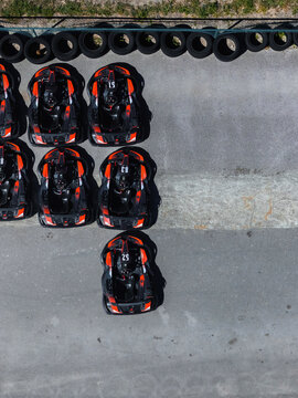Aerial view of orange and black go-karts parked on an asphalt track next to a tire barrier.