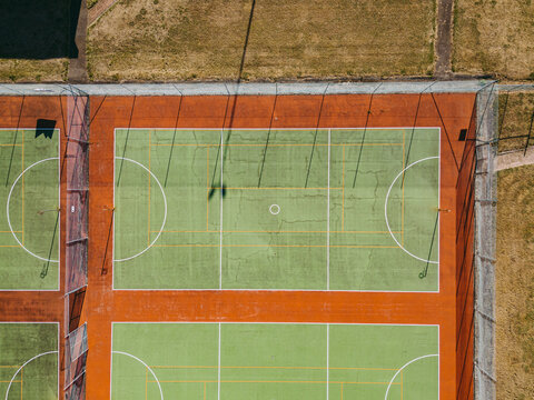 Aerial view of green and orange netball courts with white markings and chain-link fencing under bright sunlight in Devonport, Tasmania, Australia.