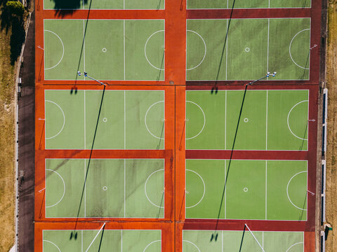 Aerial view of multiple green netball courts with red borders and long shadows from light poles in Devonport, Tasmania, Australia.
