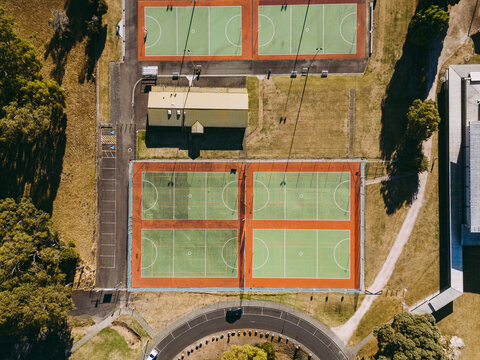 Aerial view of green and red outdoor netball courts surrounded by lush trees and a small building in Devonport, Tasmania, Australia.